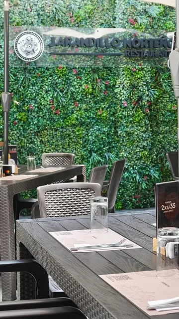 Mesas del restaurante junto al jardín vertical y al letrero de Jarandillo Norteño